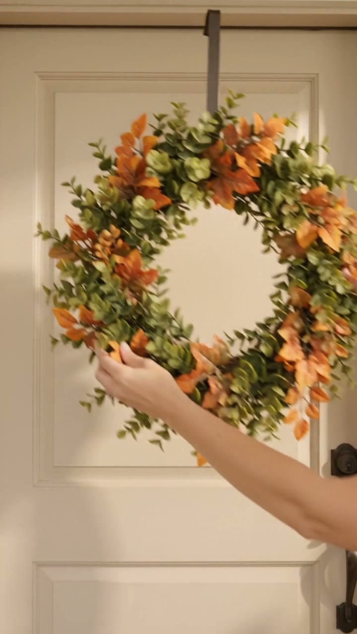 Video shows a plain front door then hands hanging a 26-inch orange boxwood wreath with autumn accents.